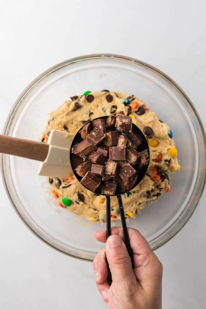 adding chopped up candy bars to cookie dough in a mixing bowl