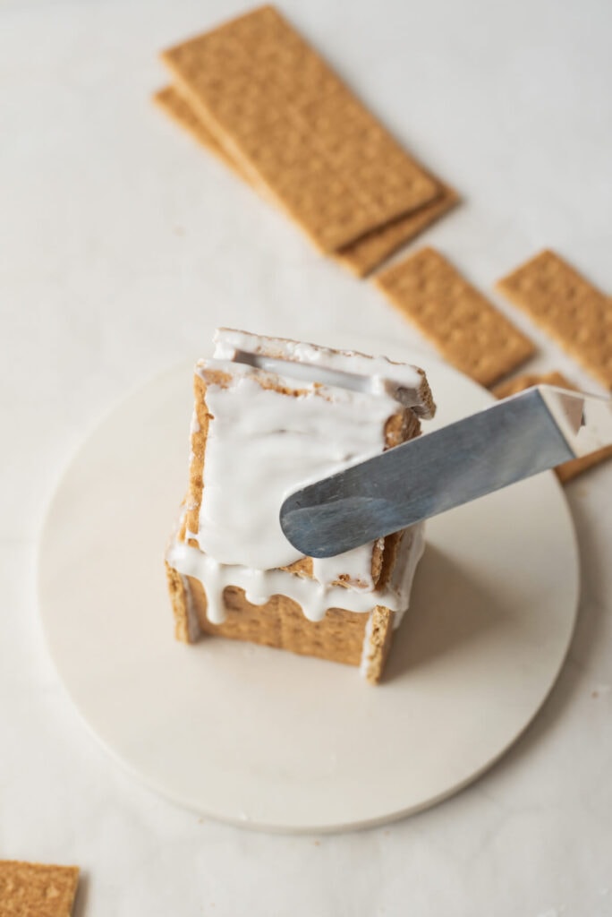 spreading icing on top of a gingerbread house roof