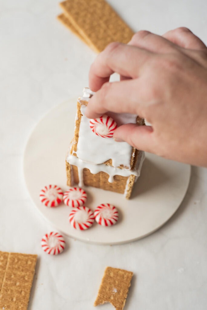 decorating a graham cracker gingerbread house with peppermints