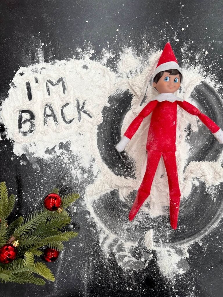 Elf on the Shelf making snow angels in flour with a note that says "I'm back"