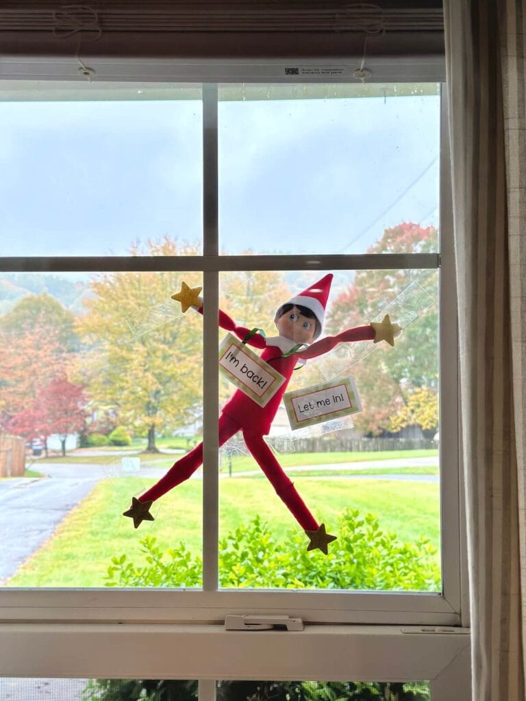 Elf on the Shelf stuck outside a window with a note that says let me in