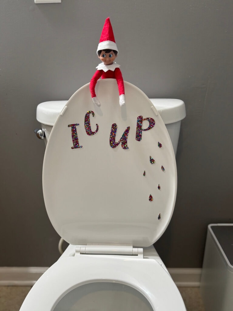 elf on the shelf with stickers I C U P on the back of a toilet