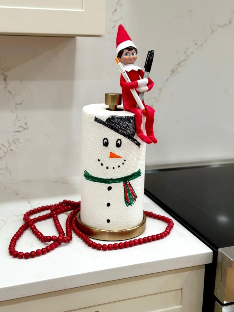 Elf on the Shelf drawing a snowman on a roll of paper towels