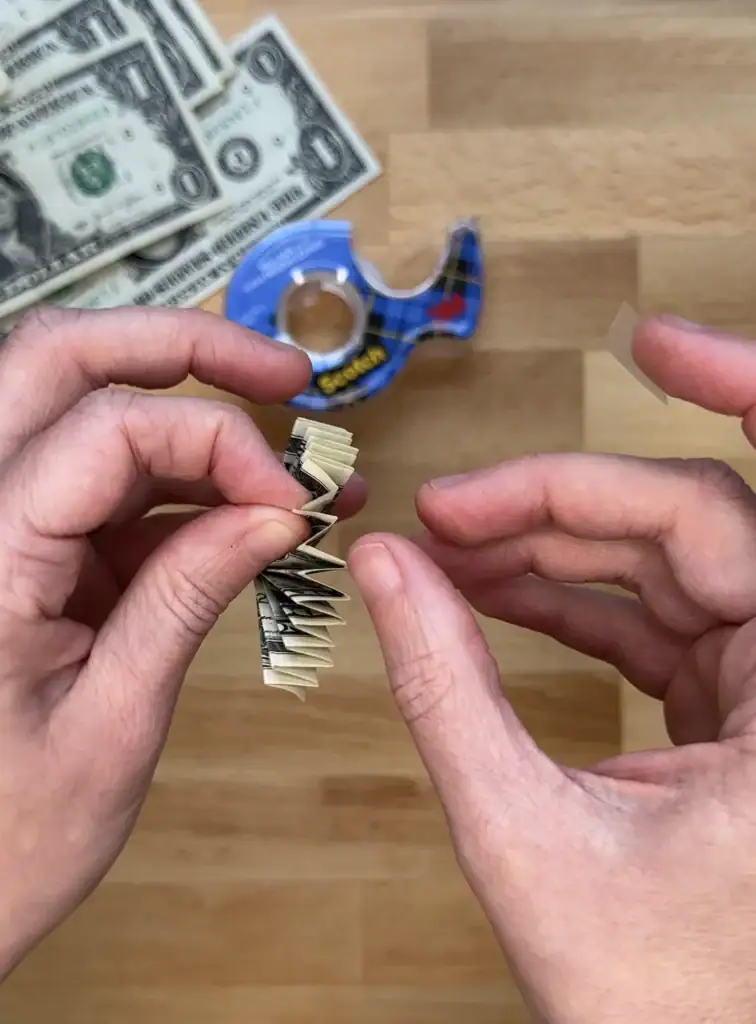 taping a folded dollar bill for a flower money lei
