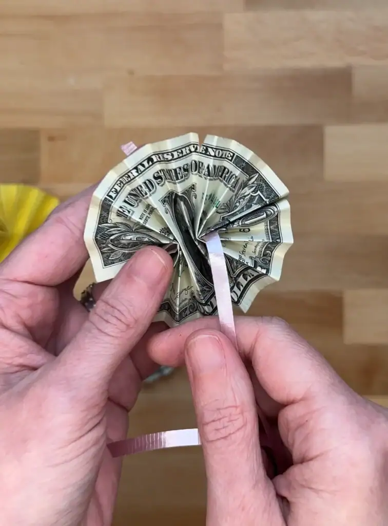 inserting curling ribbon through a fan folded dollar bill
