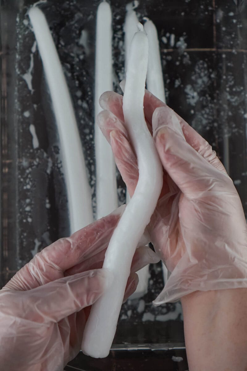 using gloved hands to shape white taper candles into a wavy shape