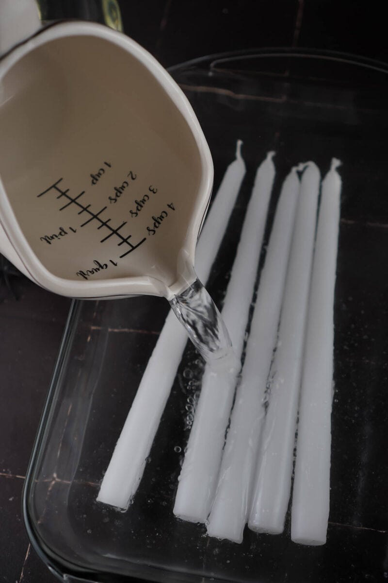 pouring water into a glass baking dish with white taper candles