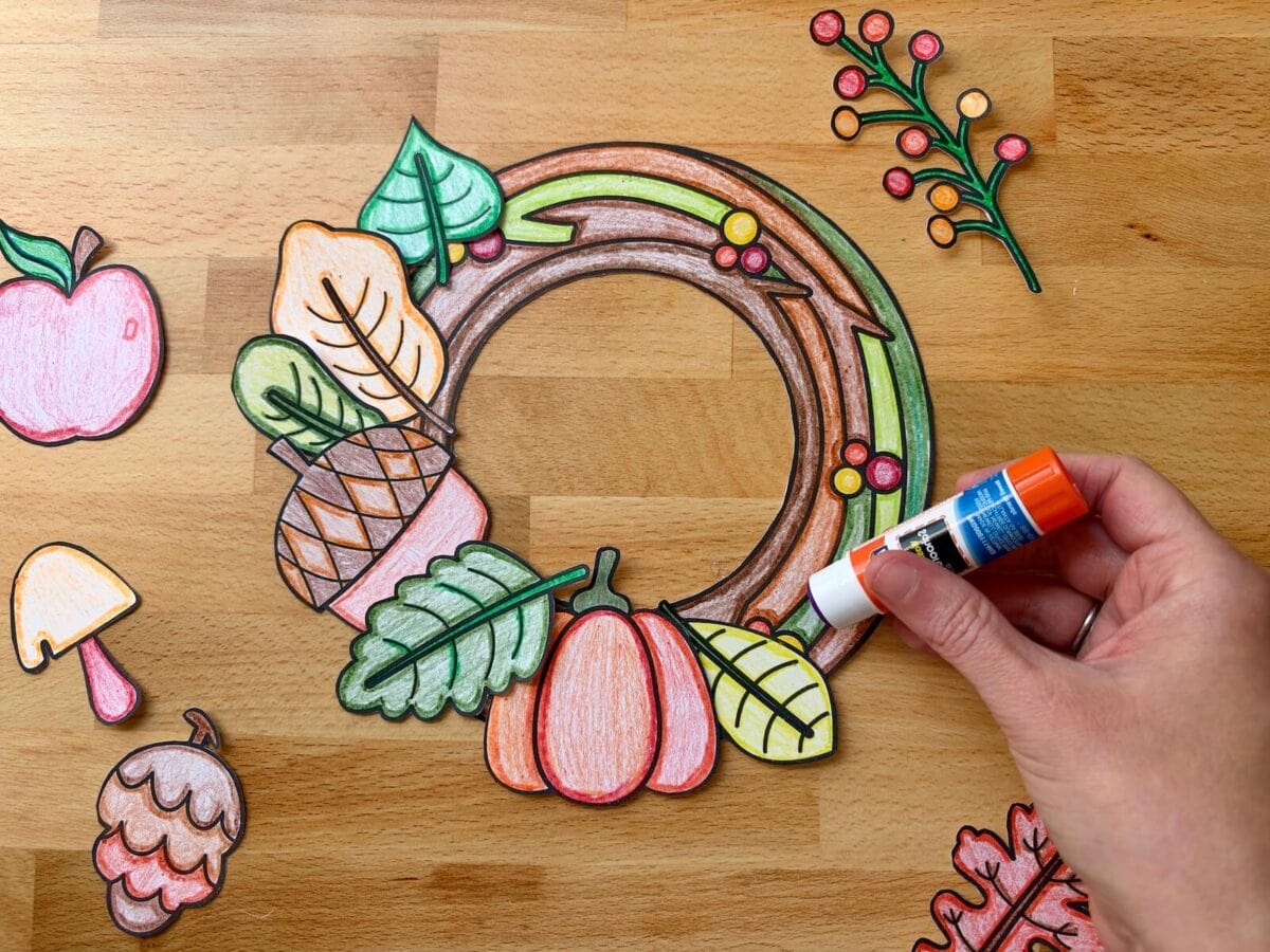 gluing colored Fall leaves onto a wreath with a glue stick